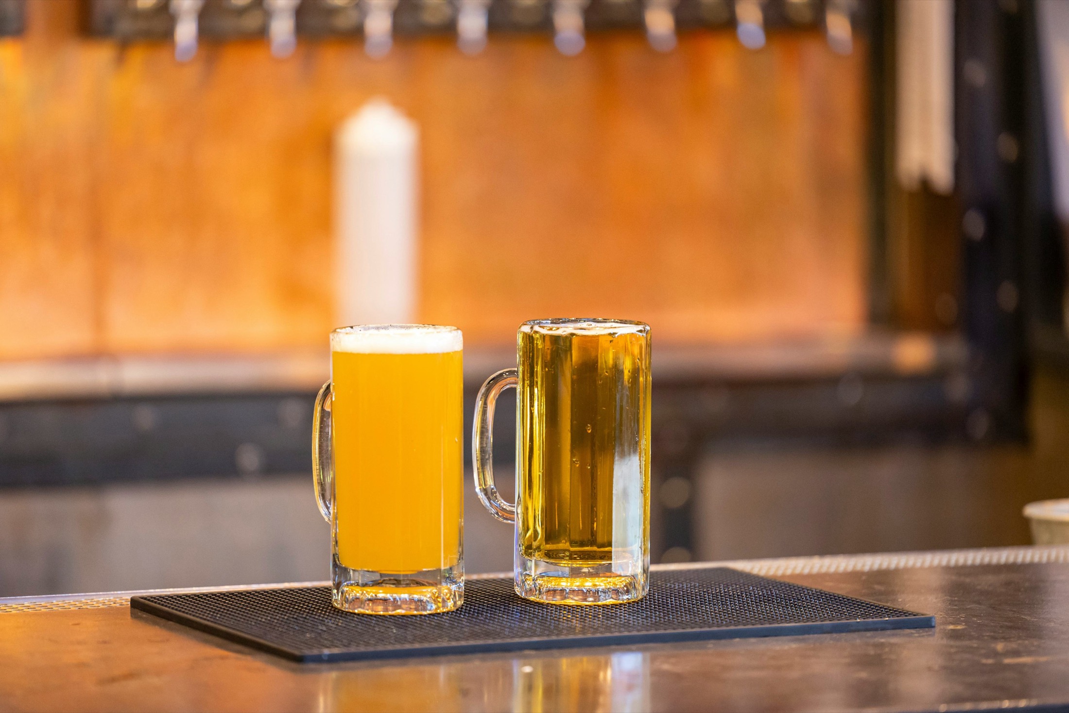 Two mugs of beer on a bar mat