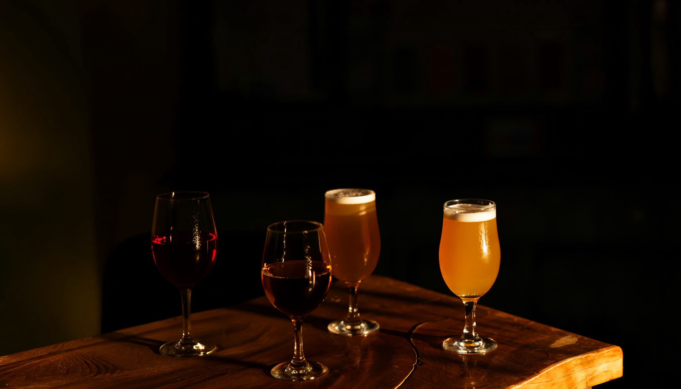Two glasses of wine and two of beer on a dark wooden table