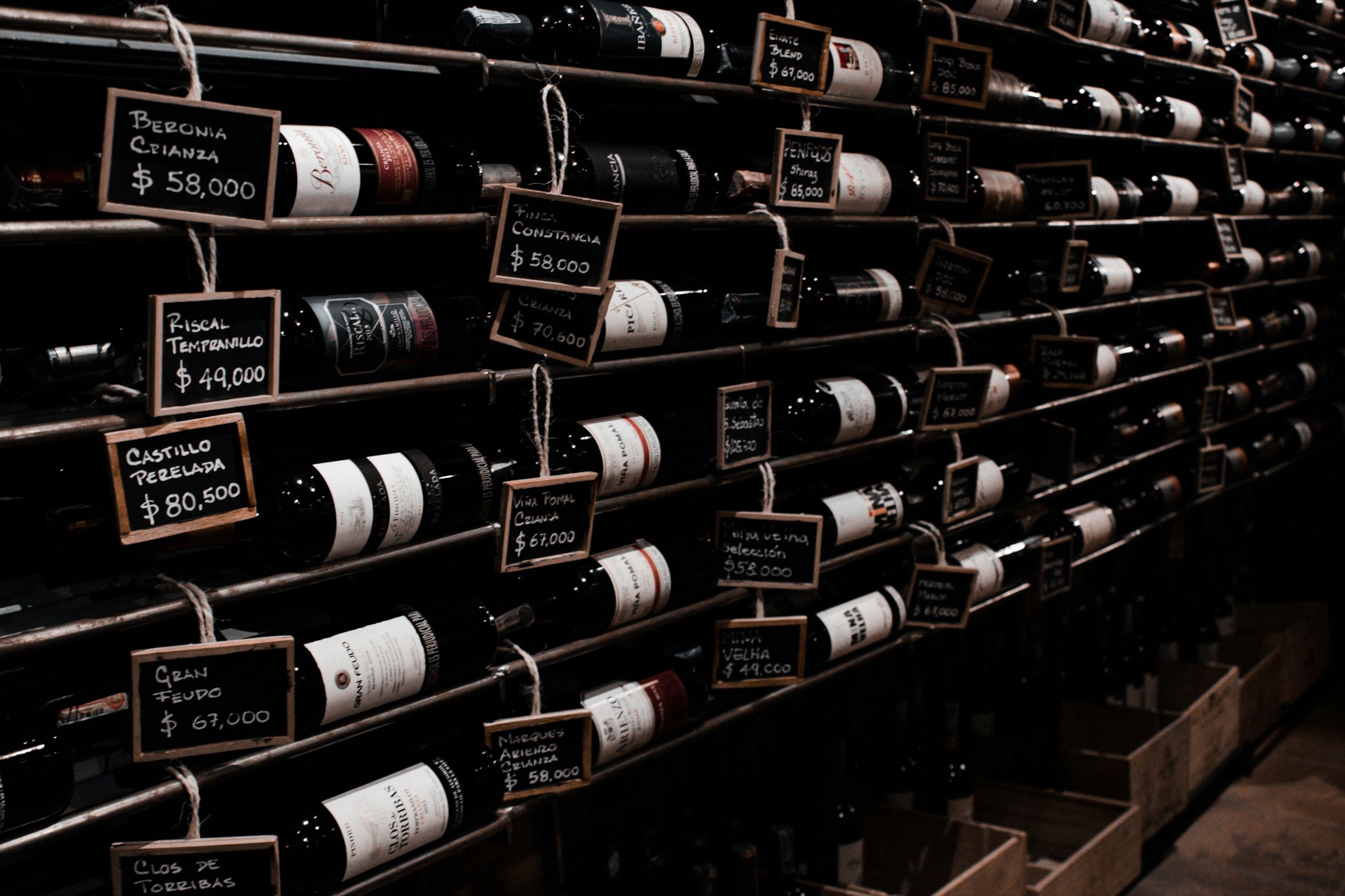 A wall of wine bottles, each with a chalkboard price tag